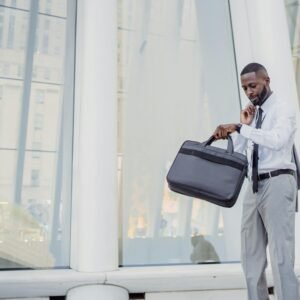 Professional man checking time with wristwatch while holding a laptop bag outside modern office.