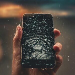 A person holds a smartphone with raindrops on screen, emphasizing water resistance.