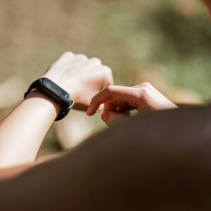 From behind crop anonymous sportswoman checking notifications on modern fitness tracker while training against blurred nature background on sunny weather