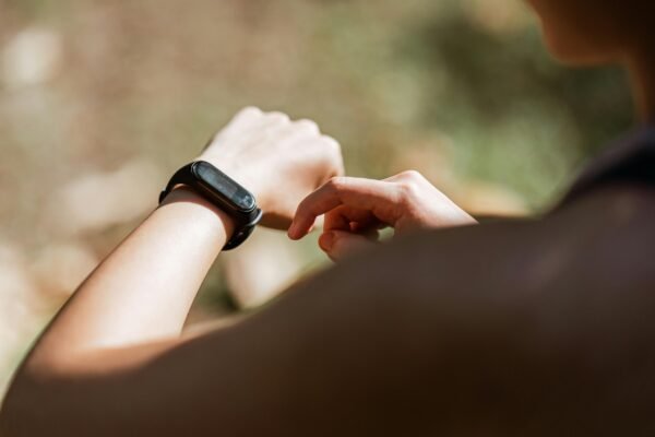 From behind crop anonymous sportswoman checking notifications on modern fitness tracker while training against blurred nature background on sunny weather