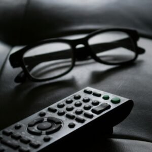 Close-up of eyewear and a TV remote on a dark leather couch, ideal for home lifestyle themes.